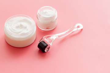 Dermaroller for home cosmetologic procedure near creams on pink background copy space