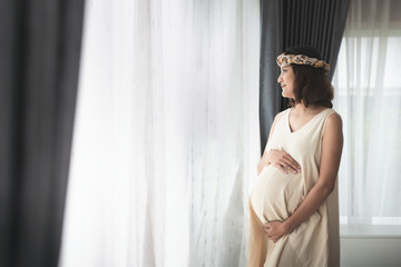Pregnancy, Pregnant woman with big belly in Maternity Dresses standing near window at home. happiness of motherhood preparation and expectation with copy space concept.