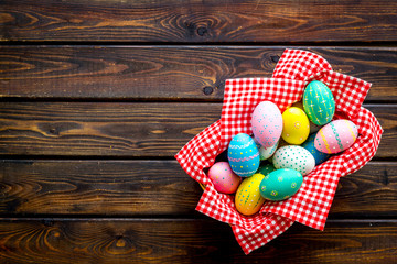 Basket with painted eggs for Easter dinner on dark wooden desk top-down copy space