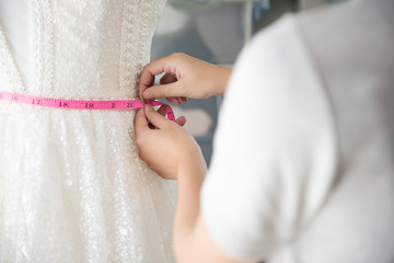 Designer woman's hands measuring the wedding dress with measuring tape at tailor shop. Body of...