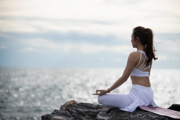 Naklejka na ściany i meble Asian young woman practicing yoga in sukhasana exercise while looking out to the sea.