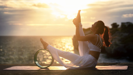 Young woman exercise yoga in nature sea sunset view. Modified Yoga Poses with Yoga Wheel, Stretching & Strengthening Exercises with advanced yoga, Relaxation & Health care concept.