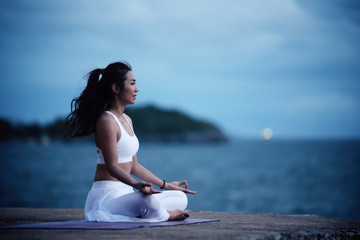 Asian young woman practicing yoga in sukhasana exercise while looking out to the sea.