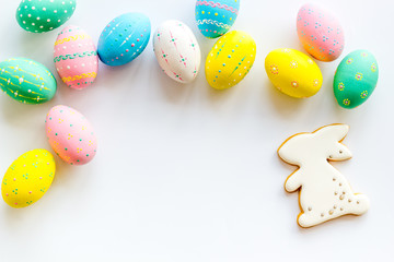 Easter symbols. Painted eggs and bunny gingerbread on white desk top-down frame copy space