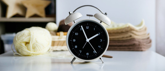 Clock alarm on a white table, on a knitting background. Concept time for knitting, hobby.