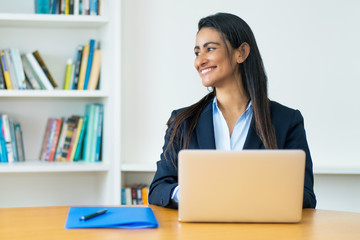 Laughing latin american mature businesswoman with blazer at computer