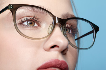 Close-up portrait of attractive young woman in glasses on blue background