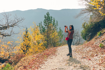 Woman is taking a nature landscape photo while hiking on the hill in autumn.