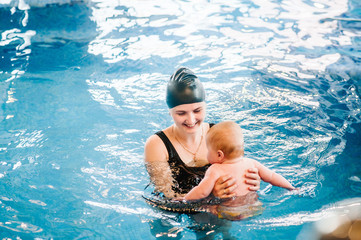 Young mother, swimming instructor and happy little girl in paddling pool. Teaches infant child to swim. Enjoy first day of swimming in water. Mom holds hand child preparing for diving. doing exercises