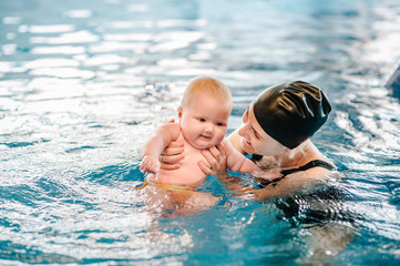 Young mother, swimming instructor and happy little girl in paddling pool. Teaches infant child to swim. Enjoy first day of swimming in water. Mom holds hand child preparing for diving. doing exercises