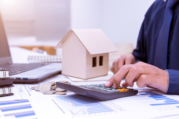 The hands of architects are pushing the calculator, calculating house design blueprint as a business and financial investment.Coin,a model of a wooden house.Planning of the construction of a house.