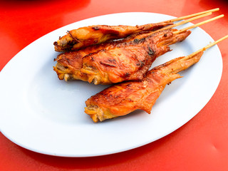 Grilled chicken wings that are skewered for easy carrying, placed on a blue plate at a street restaurant in Thailand