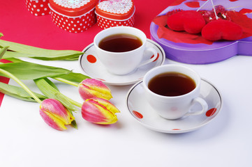 Tea for two. Two cups of tea and a bouquet of tulips on a table with a white tablecloth.