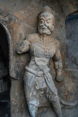 Fototapeta na wymiar Muscular warrior carved in limestone. Figure is protecting a cave door. Wei style grotto at Longmen Grottoes, Luoyang, Henan province, China
