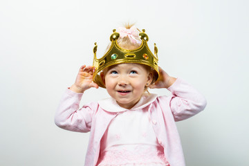 Little child girl in a dress tries on a crown on a light background. Concept little princess, dream