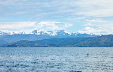Beautiful natural background with snowy mountain peaks and forested hills on the shore of the Chivyrkuisky Bay of Lake Baikal on a June day