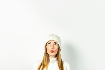 Fototapeta premium Young woman with a pensive face in a hat and sweater on a white background. Concept winter, autumn, stylish, Christmas, New Year, surprise, shock, planning, dream. Banner