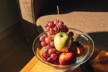 Glass bowl of variety of fruits on wooden table in warm light.