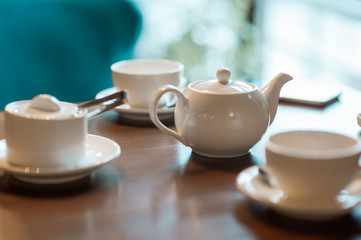 White cups and a white teapot on a table in a cafe. A mobile phone lies next to the cup.