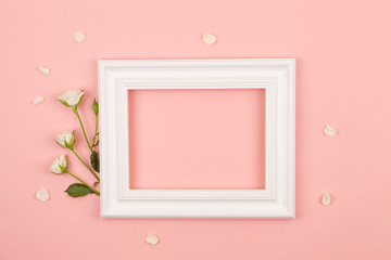 White photo frame and rose flowers on a pink background. Flat lay composition