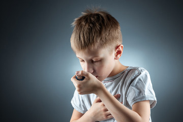 Portrait of a boy using an asthma inhaler to treat inflammatory diseases, shortness of breath. The concept of treatment for cough, allergies, respiratory tract disease.