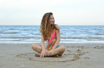 Pretty beautiful woman in pink bikini relaxing on the beach with heart love shape on the sand, Valentines and summer holiday concept