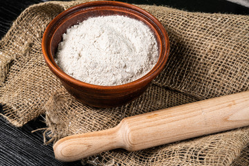 Flour in bowl with ears and grains on sackcloth background
