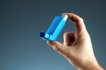 Close-up with an asthma inhaler in a male hand, asthmatic attack. The concept of treatment of bronchial asthma, cough, allergies, dyspnea. - obrazy, fototapety, plakaty