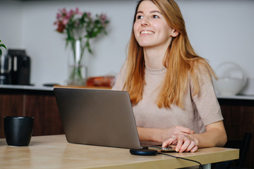 Fototapeta premium Happy woman working at the dining table, reaching for a phone on a pad