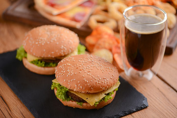 Two hamburgers, cola and other fast food on the rustic wooden table. Fast food, junk food concept.