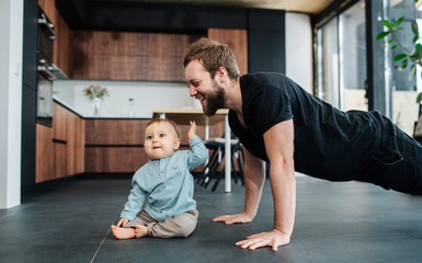 Happy father doing push upps next to his infant baby, moved and amused by him.