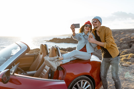 Young joyful couple making selfie portrait together while traveling by car on the rocky coast. Carefree lifestyle, love and travel concept