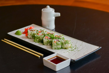 Naklejka na ściany i meble Salmon sushi rolls served on a white plate with ginger and wasabi and soy sauce in a restaurant table. Japanese cuisine.
