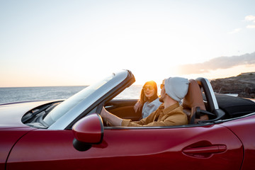 Joyful couple enjoying vacations, driving together convertible car near the ocean on a sunset. Happy vacation, love and travel concept