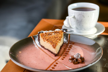 Italian traditional dessert cheesecake with walnut praline served on a pink plate with a cup of tea