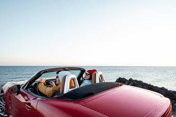 Couple driving convertible car, traveling near the ocean on a sunset, view from the backside. Happy...
