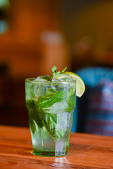 Classic fresh mojito on the table in a bar. Alcohol cocktail with ice, mint and lime on table with blurred background.
