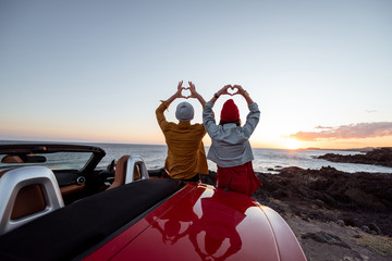 Couple enjoying beautiful views on the ocean, standing together near the car on the rocky coast,...