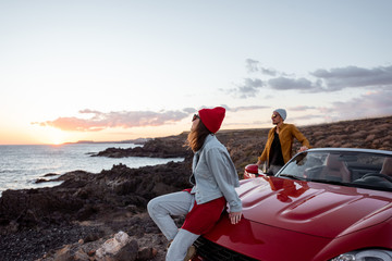 Young joyful couple having fun on the rocky coast while traveling by car on a sunset. Carefree...