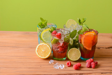 Four tropical mixed drinks, orange, lemon and raspberries cocktails over bright pastel green background.