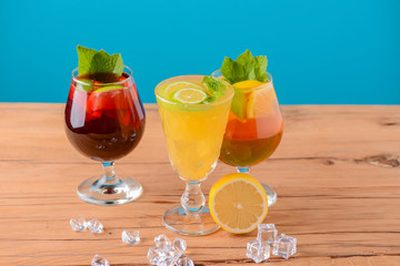 Three tropical mixed drinks with lime and lemon and mint leaves served in different glasses on rustic wooden table.