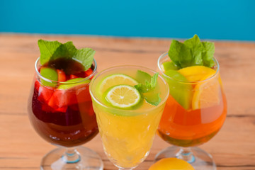 Three tropical mixed drinks with lime and lemon and mint leaves served in different glasses on rustic wooden table.