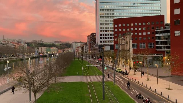 Bilbao city center with beautiful winter sunset sky; combination of modern and old architecture, green grass, public transportation system low-floor tram; developed urban environment