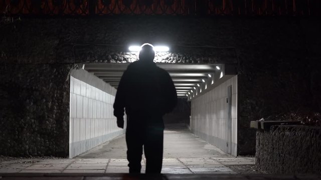 Man with backpack walking through the pedestrian underpass tunnel passage at night.