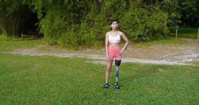 Leg Amputated Asian girl standing in a nature park after her workout session early in the morning