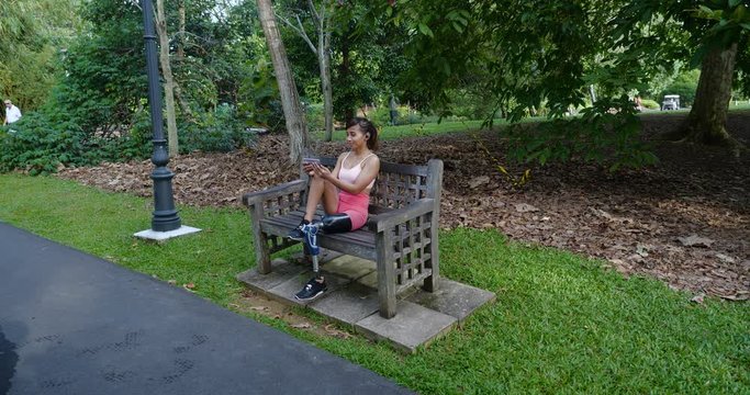 Leg Amputated Asian girl watching her handphone after working out in a park early in the morning