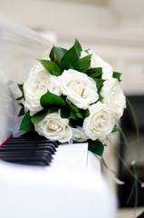 A wedding bouquet of white roses lies on the piano keys