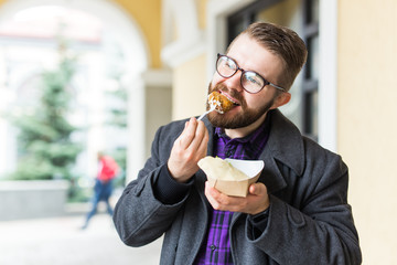 Fast food and meal concept - Young man eating take away food on the street