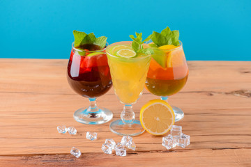 Three tropical mixed drinks with lime and lemon and mint leaves served in different glasses on rustic wooden table.