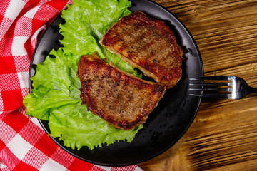 Grilled pork steaks with lettuce leaves on wooden table. Top view